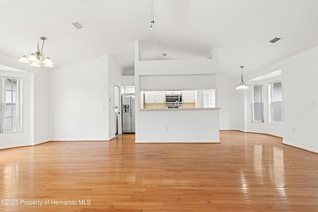 unfurnished living room featuring high vaulted ceiling, a wealth of natural light, a chandelier, and light hardwood / wood-style flooring