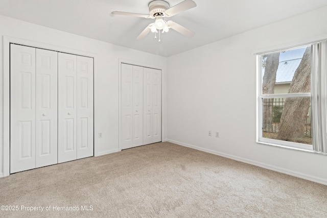 unfurnished bedroom featuring multiple closets, light carpet, and ceiling fan