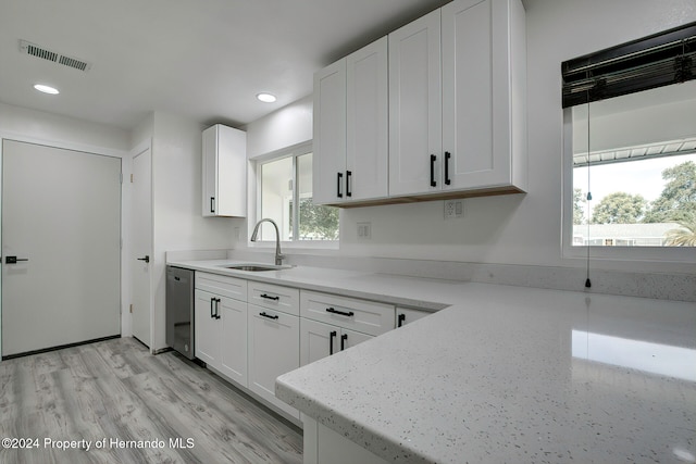 kitchen featuring light wood-type flooring, stainless steel dishwasher, a healthy amount of sunlight, and white cabinets