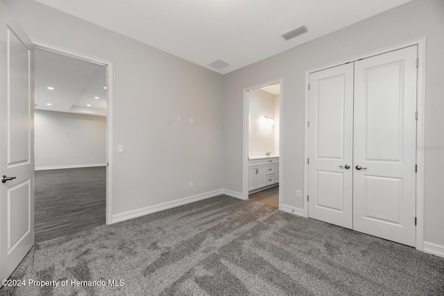 unfurnished bedroom with ensuite bathroom, dark colored carpet, and a closet