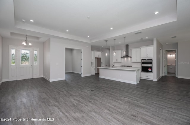 unfurnished living room featuring a chandelier, dark hardwood / wood-style floors, a raised ceiling, and sink