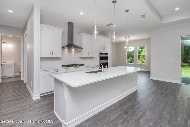 kitchen featuring white cabinetry, stainless steel appliances, wall chimney exhaust hood, and a kitchen island with sink