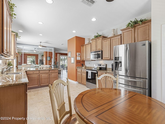 kitchen with stainless steel appliances, sink, kitchen peninsula, light stone countertops, and light tile patterned floors