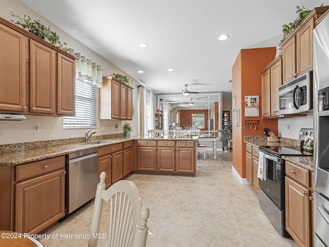 kitchen with stainless steel appliances, sink, light stone counters, and kitchen peninsula