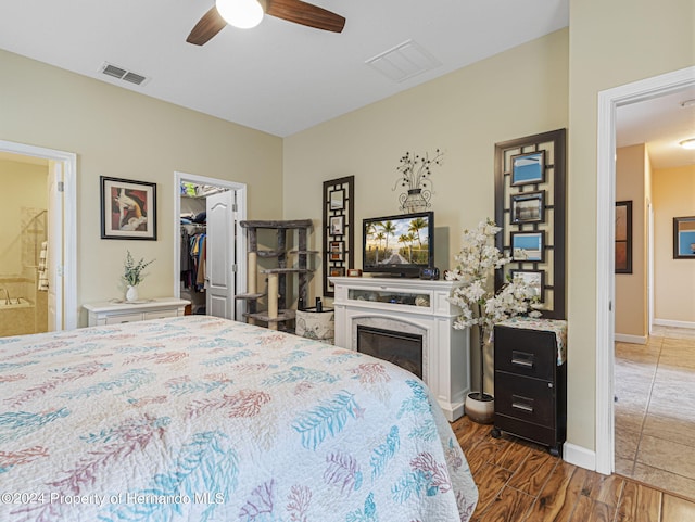 bedroom featuring a spacious closet, ensuite bath, dark wood-type flooring, a high end fireplace, and ceiling fan