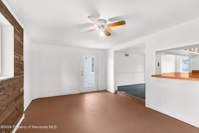 spare room featuring concrete flooring, wooden walls, and ceiling fan