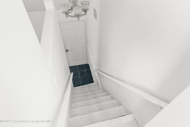 stairs with tile patterned floors and an inviting chandelier