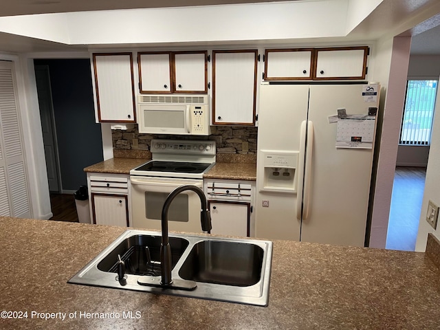 kitchen with white appliances, white cabinetry, sink, and backsplash