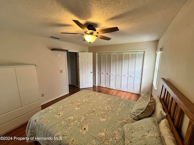 bedroom with a textured ceiling, a barn door, ceiling fan, dark hardwood / wood-style floors, and a closet