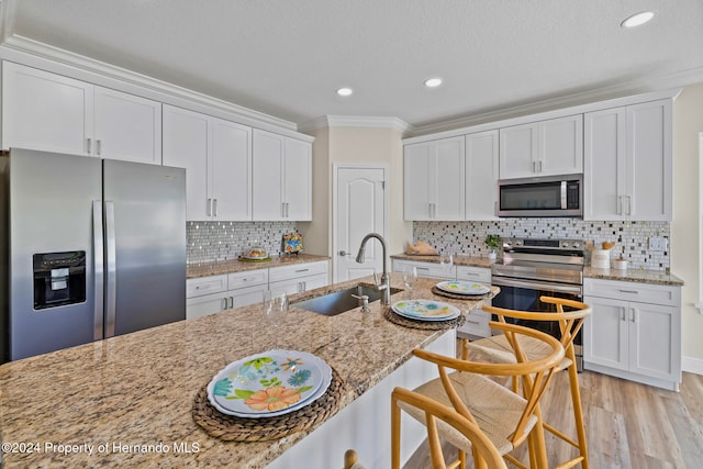 kitchen with white cabinetry, sink, light stone counters, appliances with stainless steel finishes, and ornamental molding