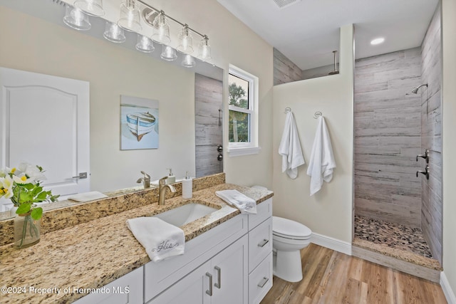 bathroom featuring wood-type flooring, vanity, toilet, and a tile shower