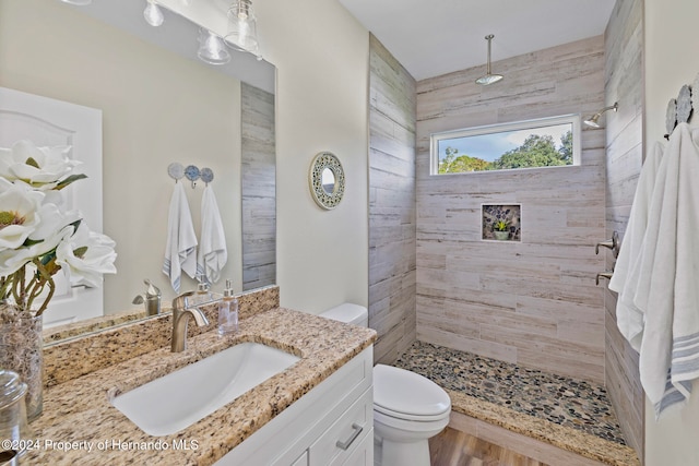 bathroom featuring hardwood / wood-style flooring, vanity, toilet, and a tile shower