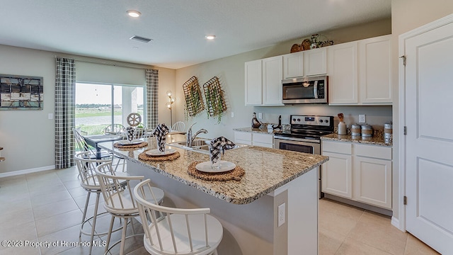 kitchen featuring stainless steel appliances, light stone countertops, white cabinetry, and a kitchen island with sink