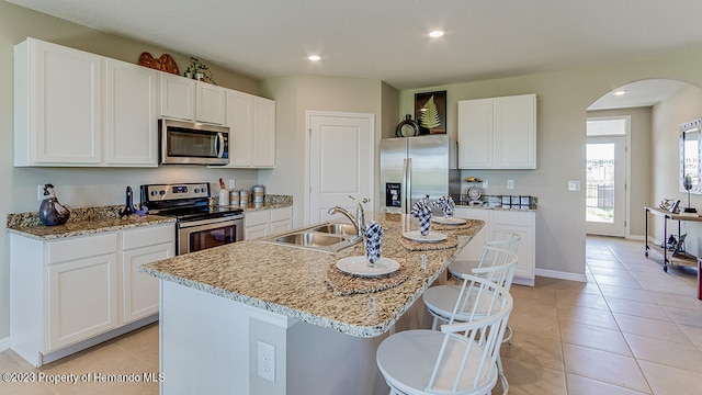 kitchen with sink, a kitchen island with sink, light stone countertops, white cabinetry, and appliances with stainless steel finishes