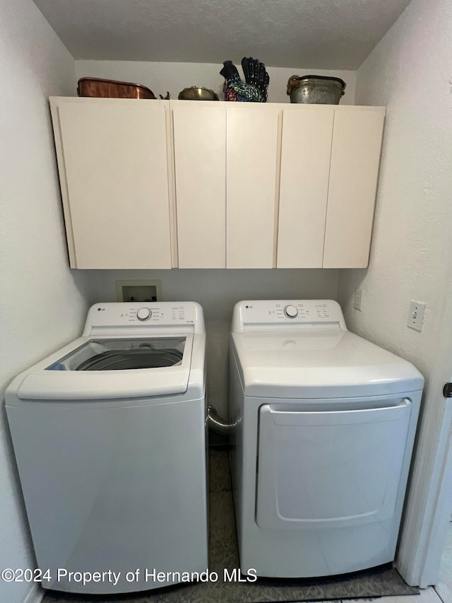 laundry area with cabinets, washing machine and clothes dryer, and a textured ceiling