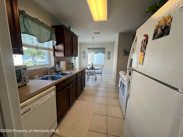 kitchen featuring dark brown cabinetry, sink, light tile patterned floors, white appliances, and decorative light fixtures