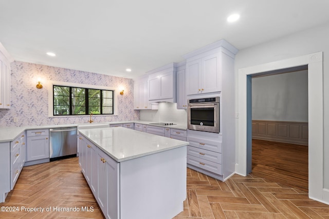 kitchen featuring light parquet flooring, light stone counters, appliances with stainless steel finishes, white cabinets, and a center island