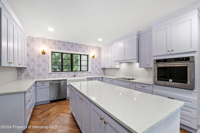 kitchen with stainless steel appliances, light stone counters, sink, parquet floors, and a kitchen island