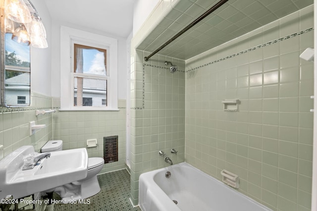 full bathroom with toilet, heating unit, tiled shower / bath combo, and tile walls