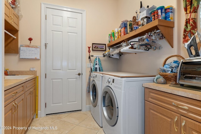 laundry area with light tile patterned floors, washing machine and dryer, cabinets, and sink