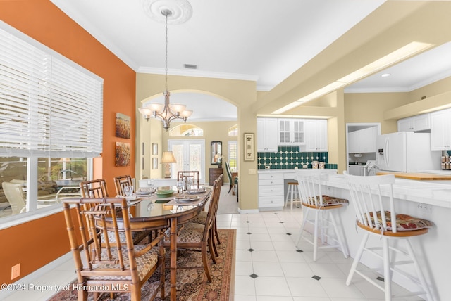 tiled dining room with an inviting chandelier, french doors, crown molding, and plenty of natural light