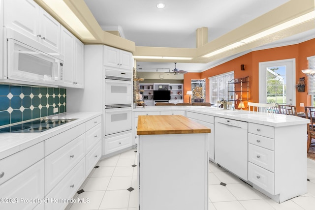 kitchen featuring kitchen peninsula, backsplash, white appliances, a center island, and white cabinets