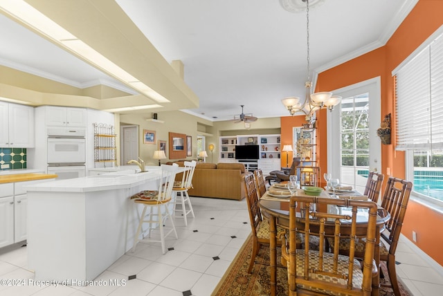 dining room with light tile patterned flooring, sink, ornamental molding, and ceiling fan with notable chandelier