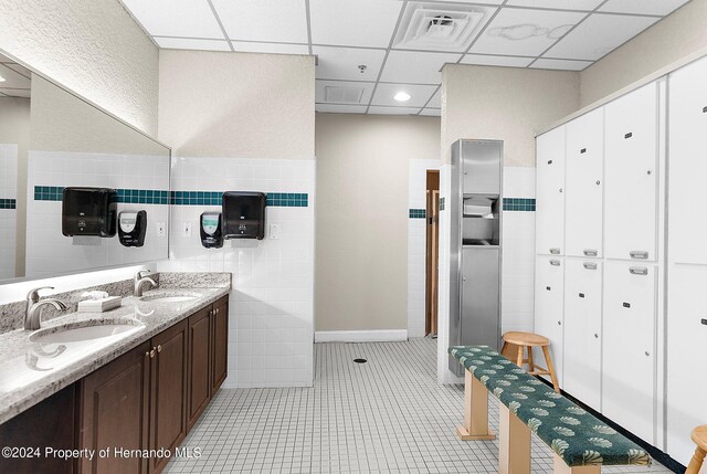 bathroom featuring vanity, tile patterned flooring, tile walls, and a drop ceiling