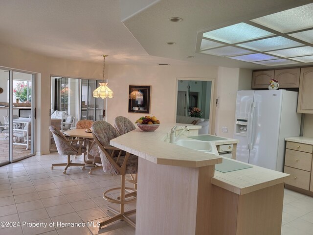 kitchen with a center island, decorative light fixtures, light tile patterned floors, white fridge with ice dispenser, and sink