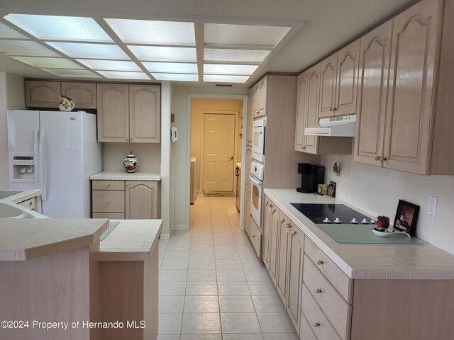 kitchen featuring white appliances, backsplash, tile counters, light brown cabinets, and light tile patterned flooring