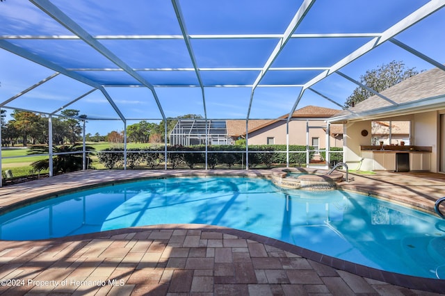 view of pool featuring exterior kitchen, a patio area, glass enclosure, and an in ground hot tub