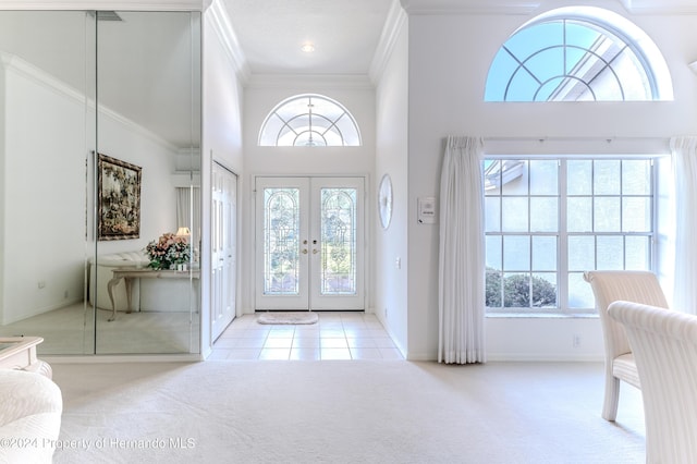 foyer with a towering ceiling, french doors, light carpet, and ornamental molding