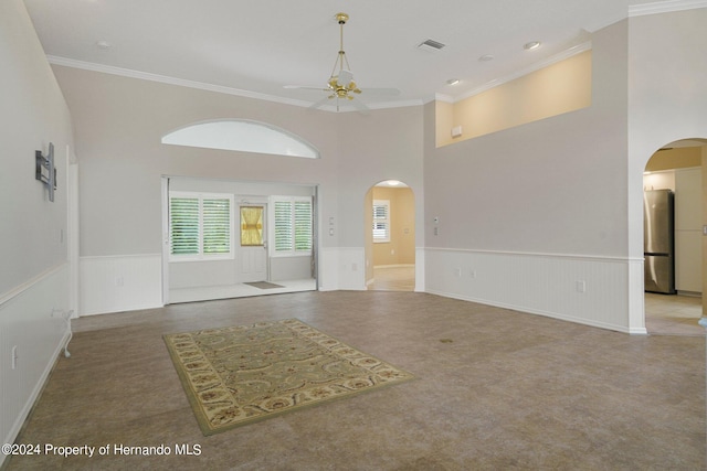 spare room featuring carpet, crown molding, ceiling fan, and a towering ceiling