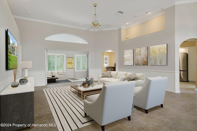 living room with a towering ceiling, ceiling fan, and crown molding