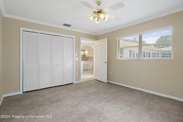 unfurnished bedroom with ceiling fan, light carpet, a closet, and crown molding