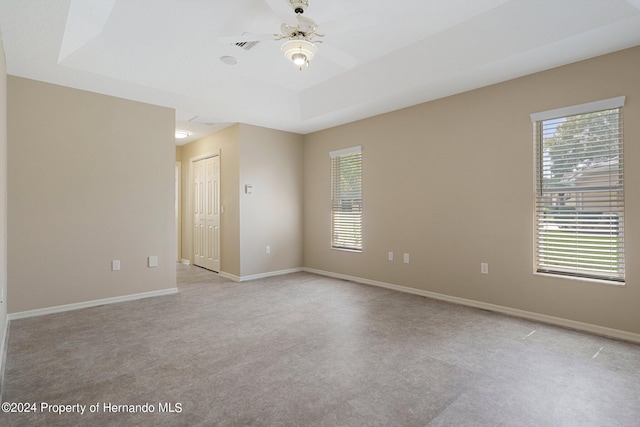 spare room with a raised ceiling, light carpet, ceiling fan, and plenty of natural light