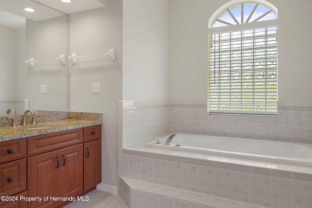 bathroom featuring a wealth of natural light, vanity, and a relaxing tiled tub