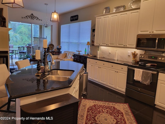 kitchen with stainless steel appliances, a center island with sink, sink, white cabinetry, and a kitchen bar