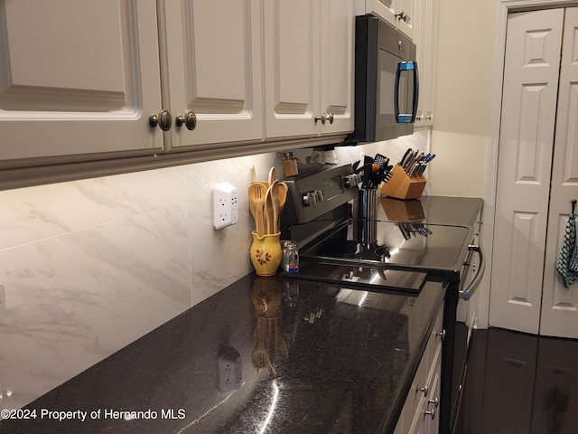 kitchen featuring white cabinetry, appliances with stainless steel finishes, backsplash, and dark stone countertops