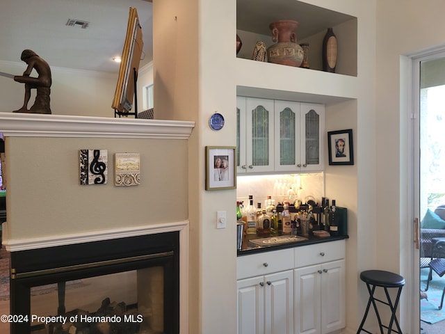 bar with white cabinets and crown molding