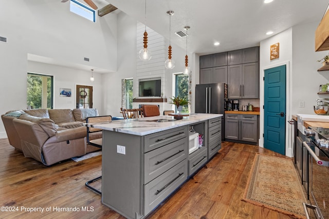 kitchen with light stone countertops, a kitchen bar, high vaulted ceiling, gray cabinetry, and pendant lighting