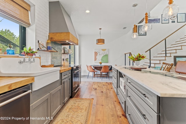 kitchen with appliances with stainless steel finishes, backsplash, hanging light fixtures, light hardwood / wood-style flooring, and gray cabinets