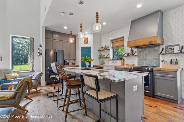 kitchen featuring stainless steel appliances, hanging light fixtures, plenty of natural light, and premium range hood