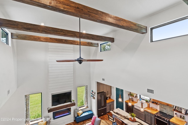 living room featuring a towering ceiling, hardwood / wood-style flooring, ceiling fan, and beam ceiling