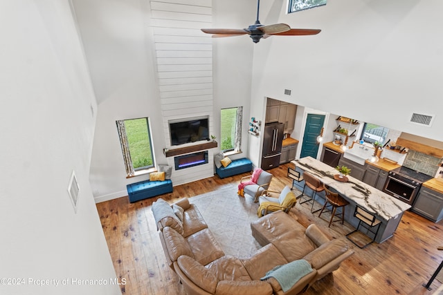 living room with a fireplace, hardwood / wood-style flooring, a high ceiling, and ceiling fan