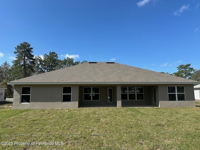 rear view of property with stucco siding, a lawn, and roof with shingles