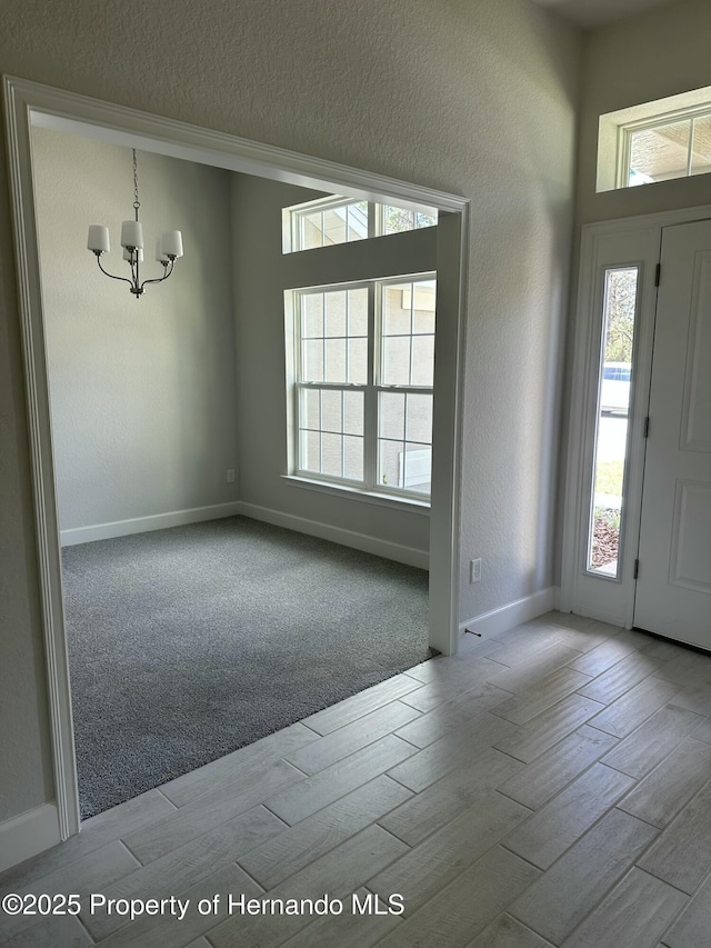 foyer featuring wood finish floors, a textured wall, baseboards, and a chandelier