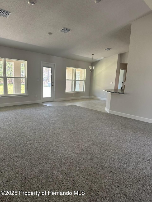 unfurnished living room with a textured ceiling, baseboards, visible vents, and light carpet