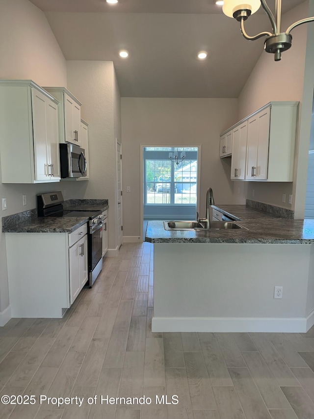 kitchen featuring light wood-type flooring, appliances with stainless steel finishes, a peninsula, an inviting chandelier, and a sink