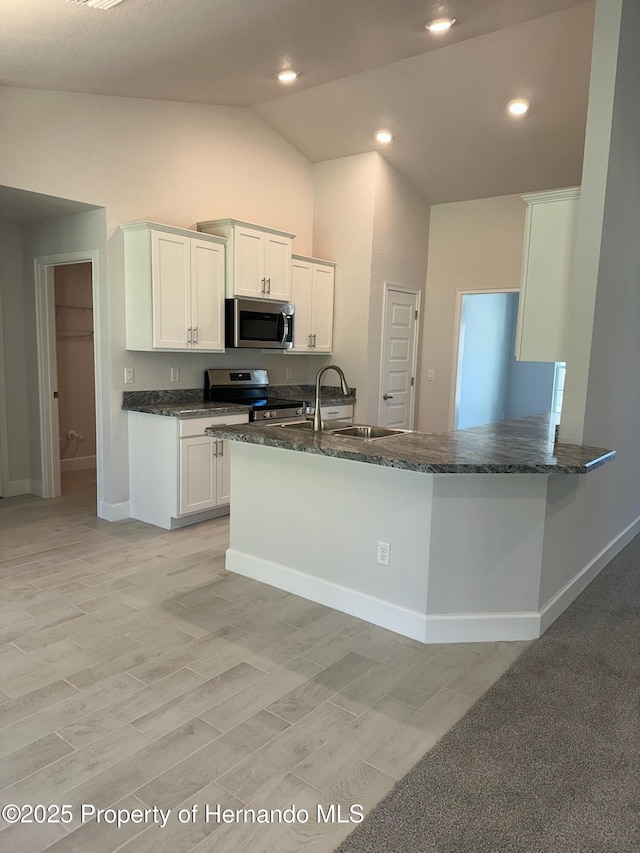 kitchen featuring dark stone countertops, a sink, stainless steel appliances, vaulted ceiling, and white cabinets